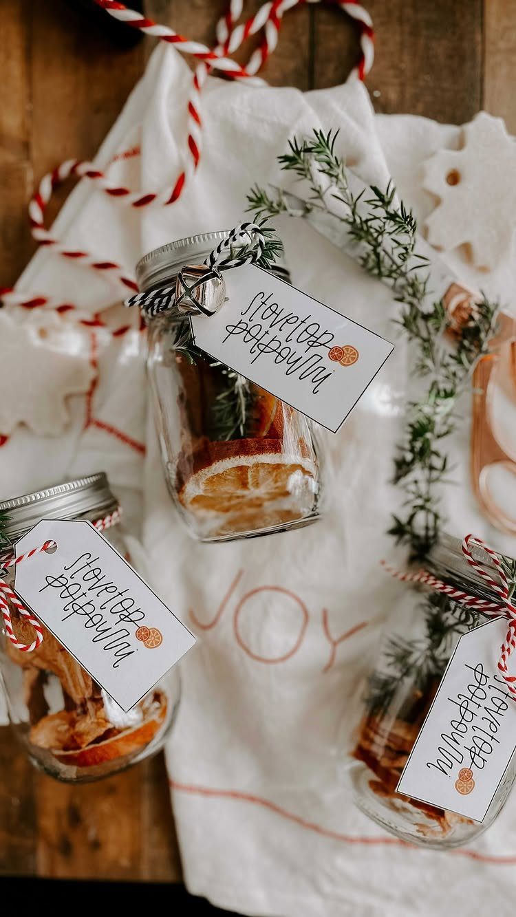 Three mason jars filled with stovetop potpourri ingredients and gift tags on white cloth.