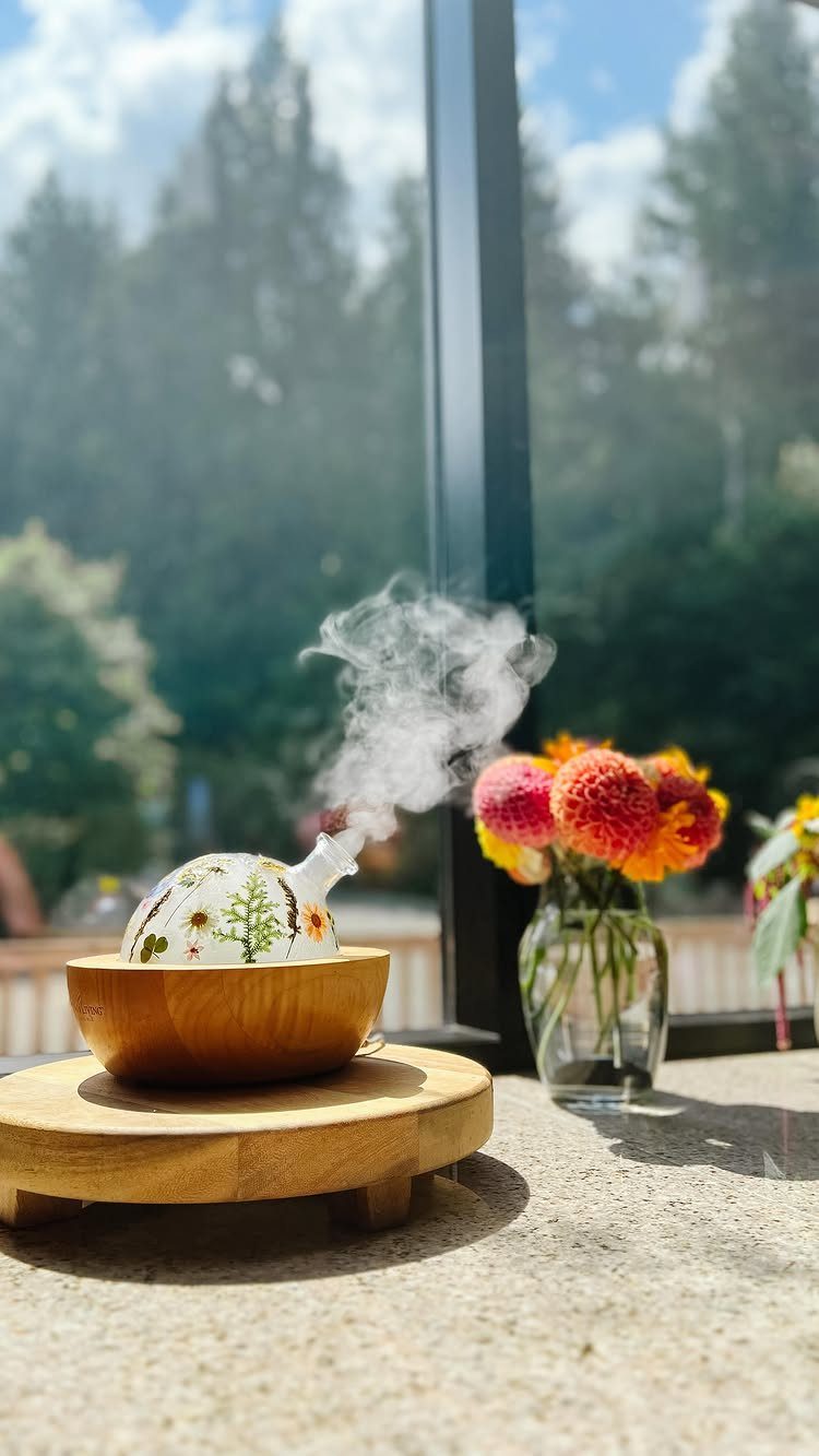 Aromatherapy diffuser with wooden base emitting mist next to yellow flowers.