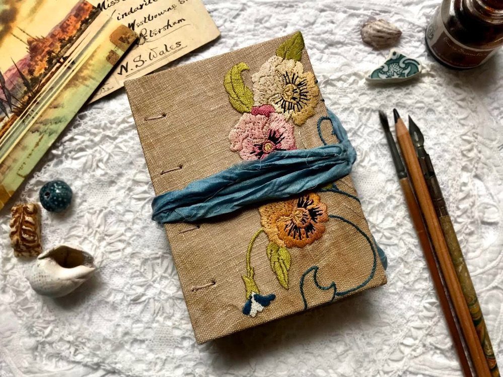 Embroidered linen journal with floral designs and a blue ribbon tie.