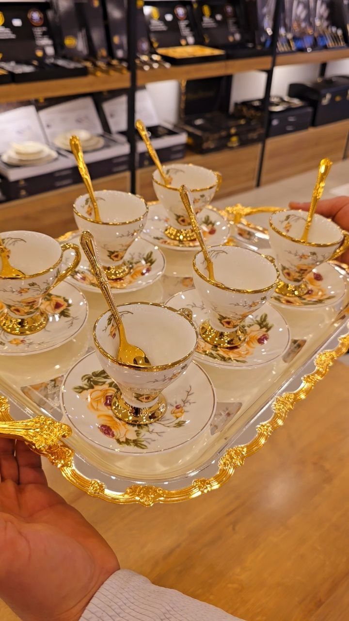Ornate white tea cups with gold rims and floral patterns on a gold tray