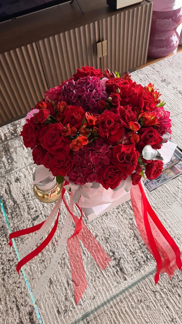 Red and pink rose bouquet with ribbons on a glass table.