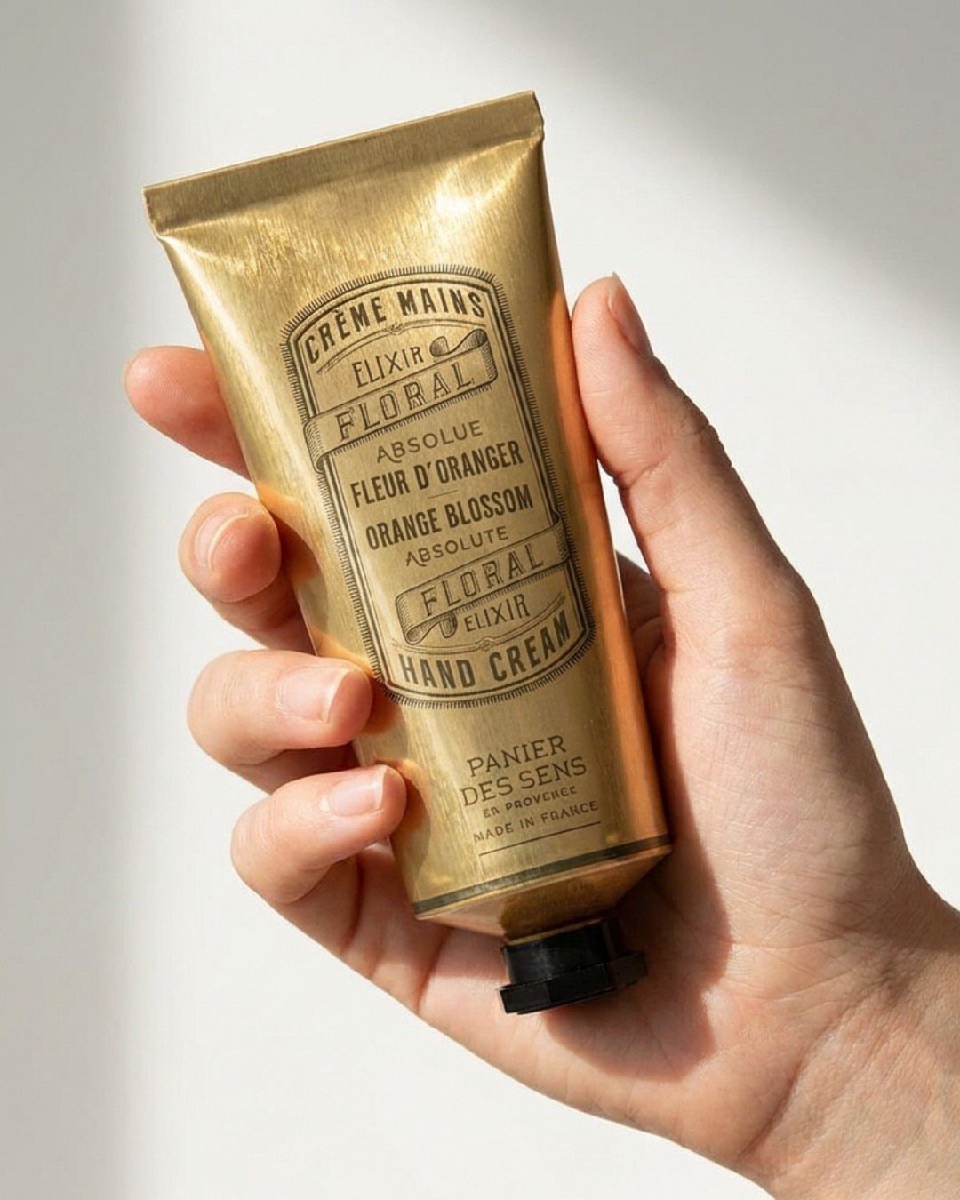 Gold tube of floral hand cream held in a person's hand