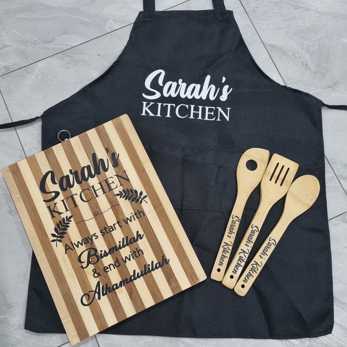 Personalized kitchen gift set featuring a black apron, wooden cutting board, and utensils.