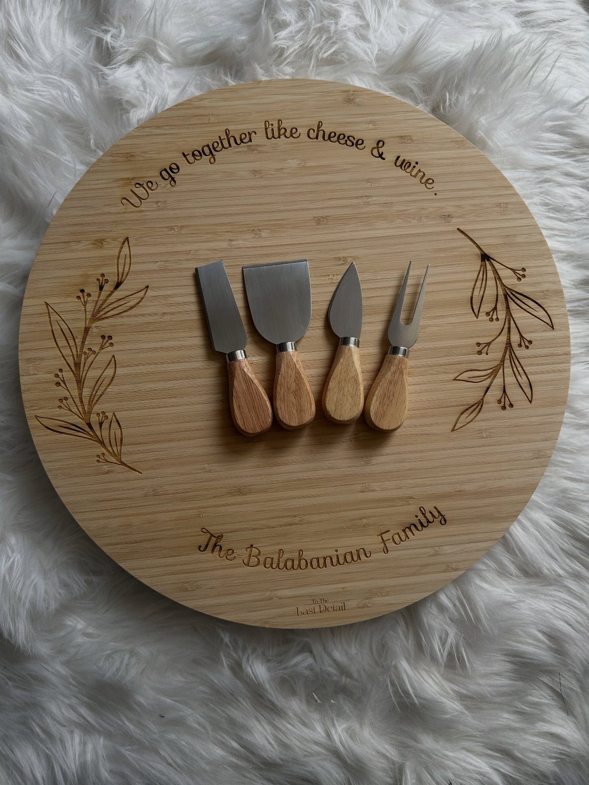 Round wooden charcuterie board with engraved family name and four cheese knives.