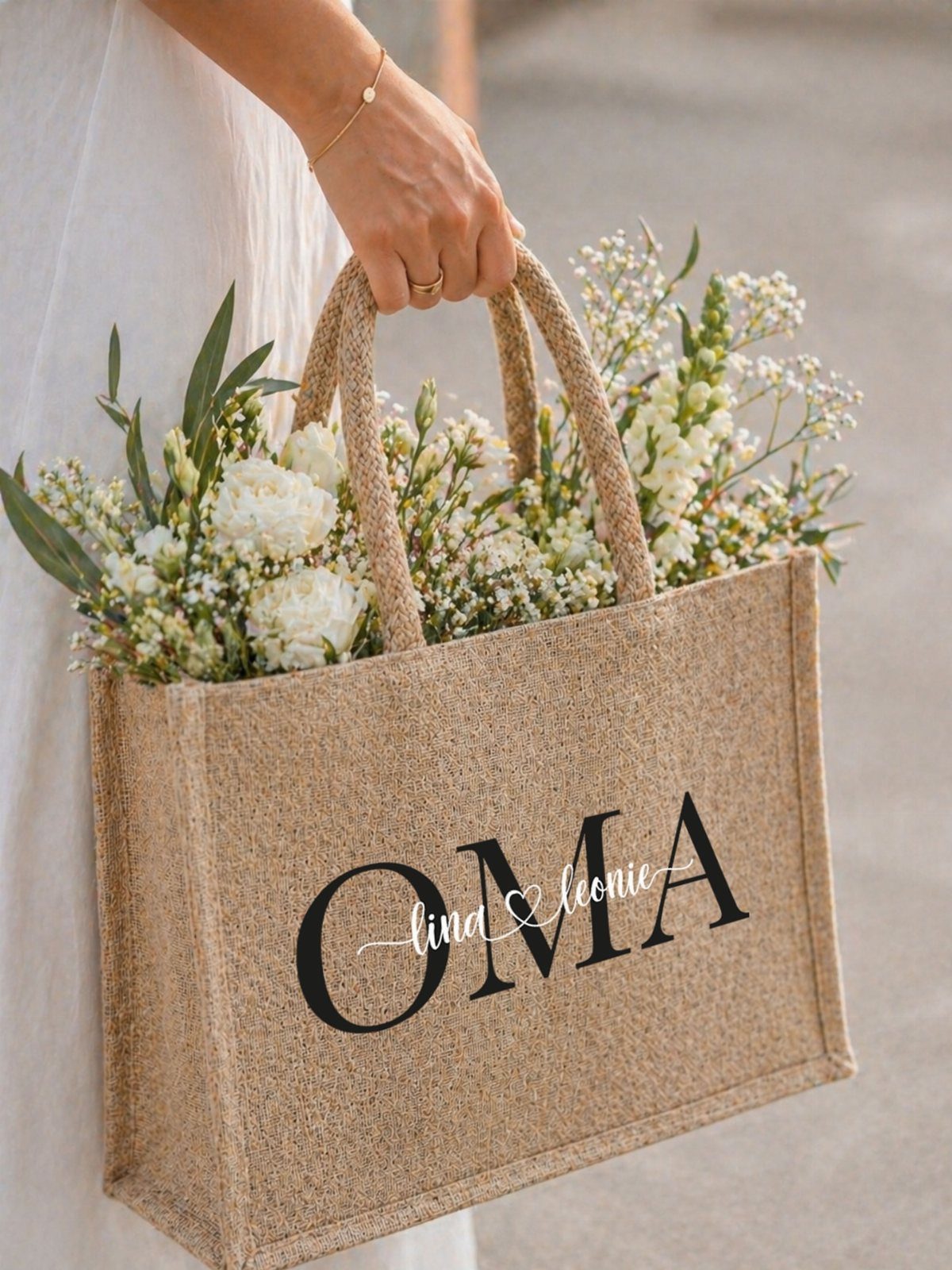 Burlap tote bag with OMA text filled with white flowers held by person