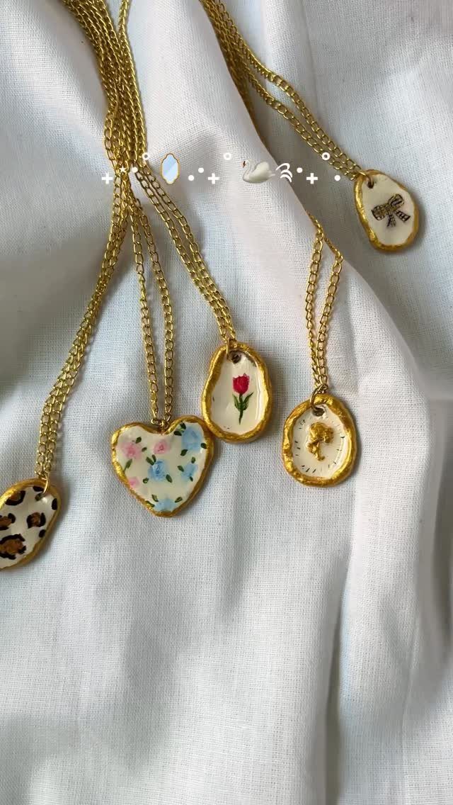 Gold chain necklaces with hand-painted white clay pendants on white fabric background