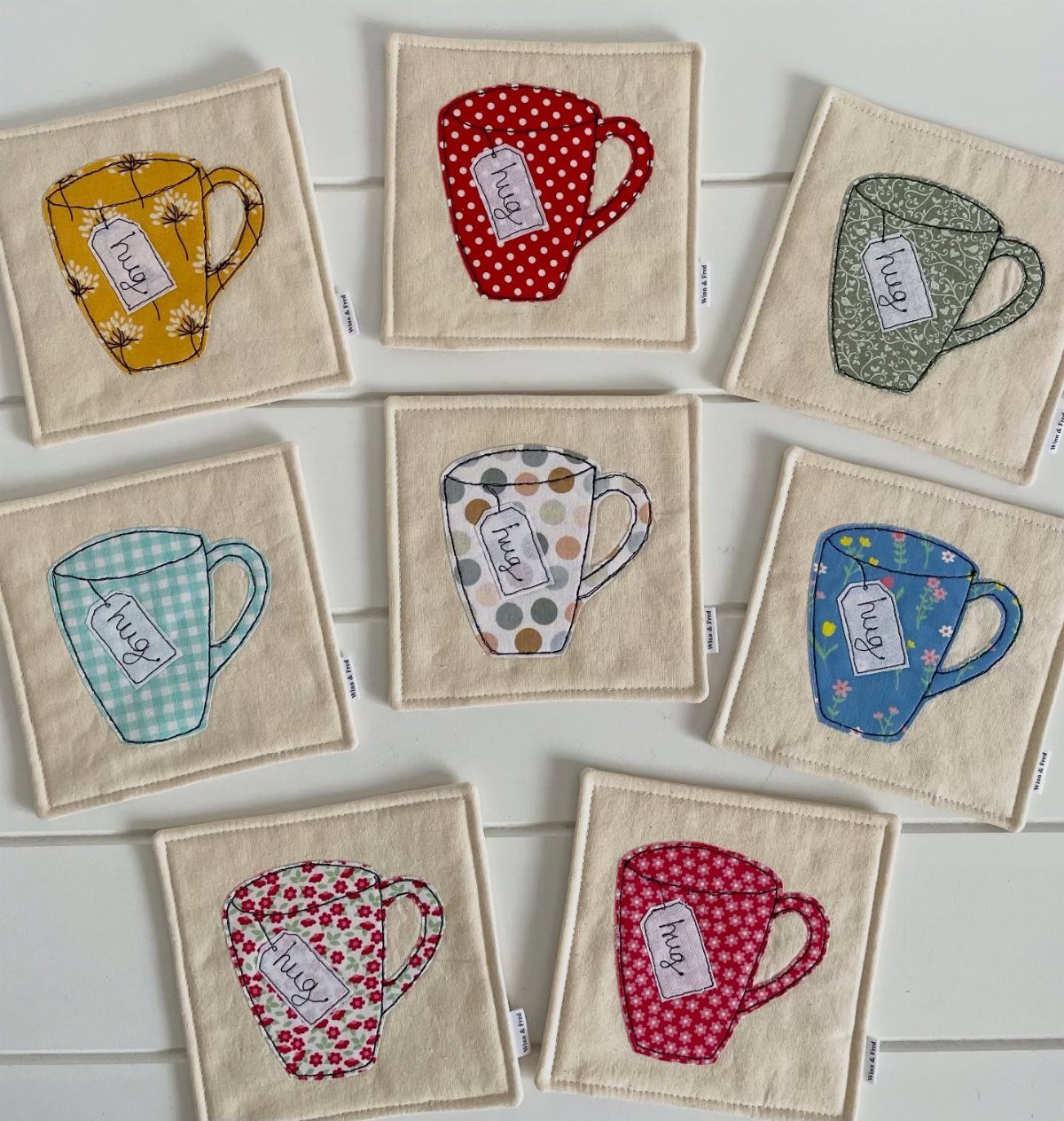 Beige fabric coasters with colorful fabric mug appliques and hug tags on white wood