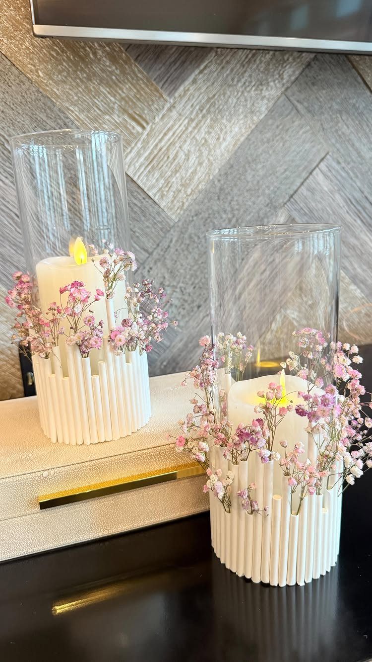 White ribbed candle holders with lit candles and pink flowers in glass cylinders.