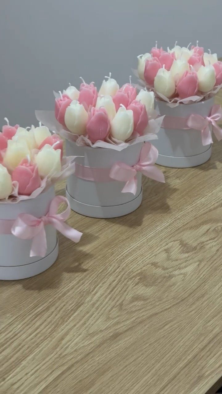 Tulip-shaped pink and cream candles arranged in white gift boxes with pink ribbons.