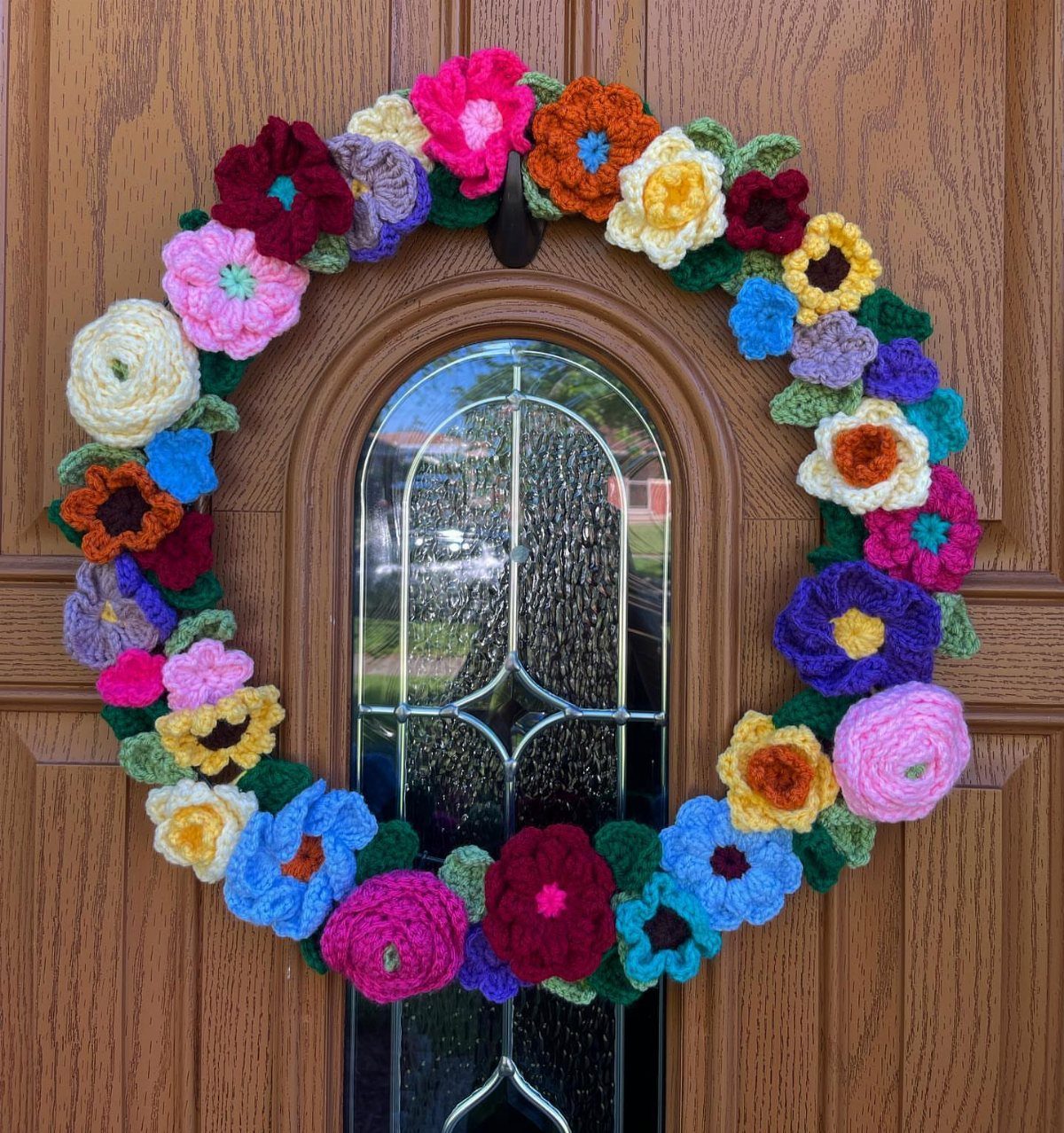 Colorful crochet flower wreath hanging on a brown wooden door with glass window