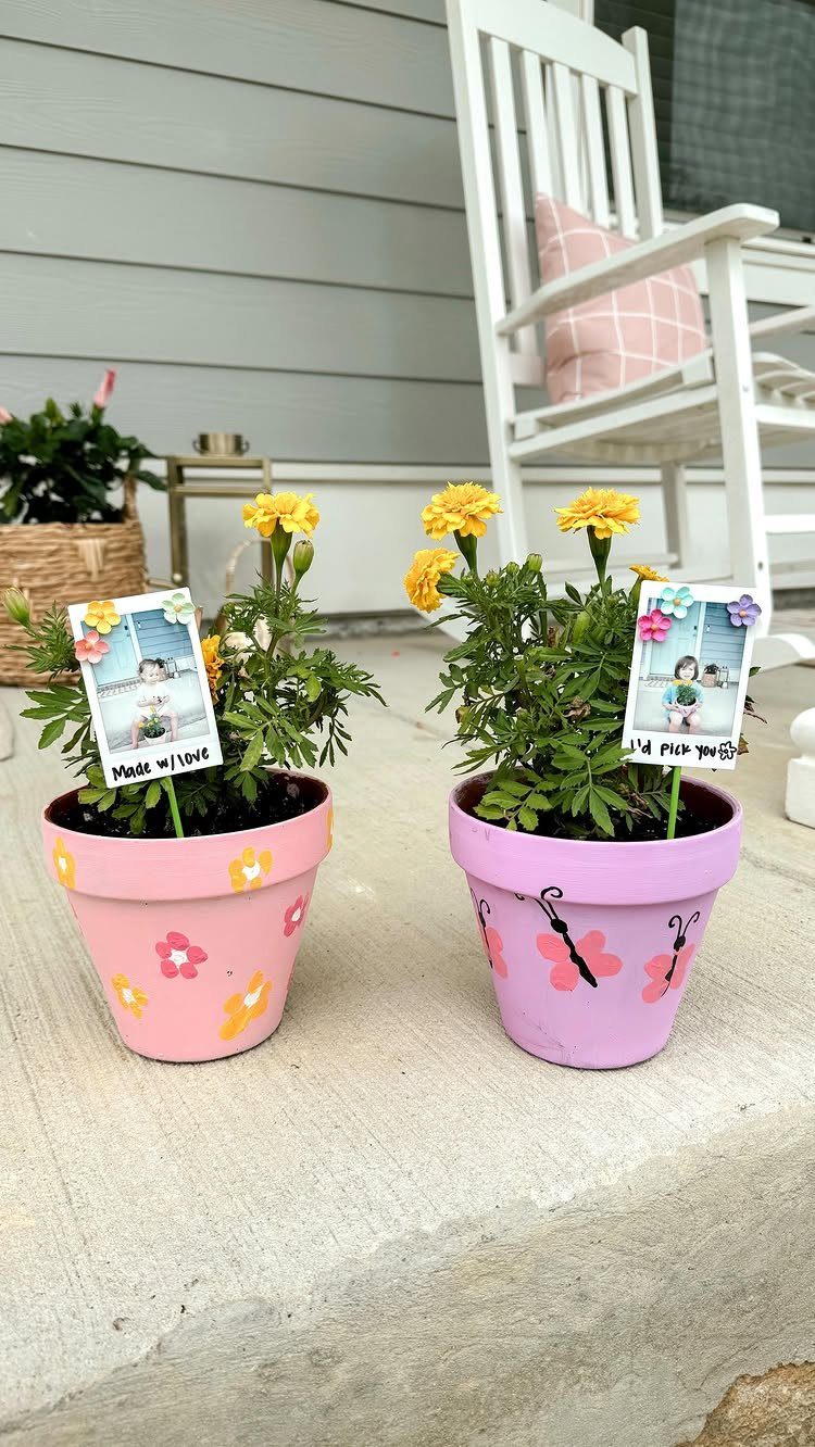 Two hand-painted pink and purple flower pots with yellow marigolds and photo cards.