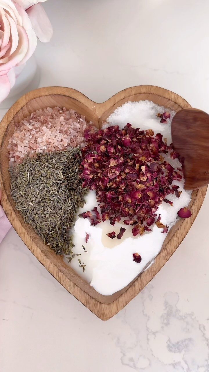 Heart-shaped wooden bowl filled with bath salts, dried herbs, and red rose petals.