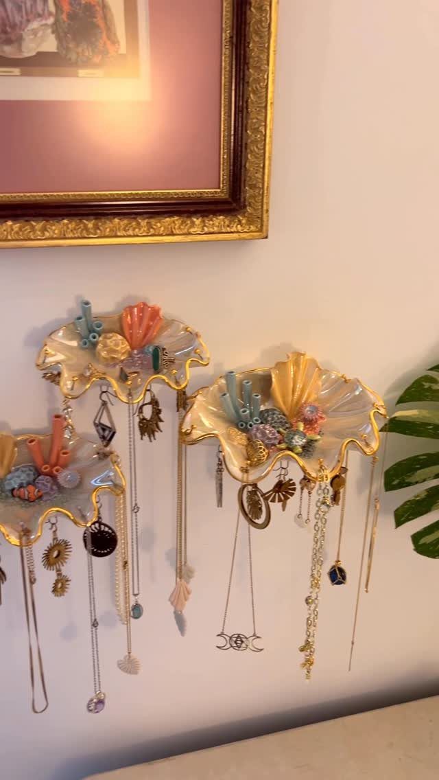 Shell-shaped ceramic wall organizers holding various gold necklaces and jewelry pieces.