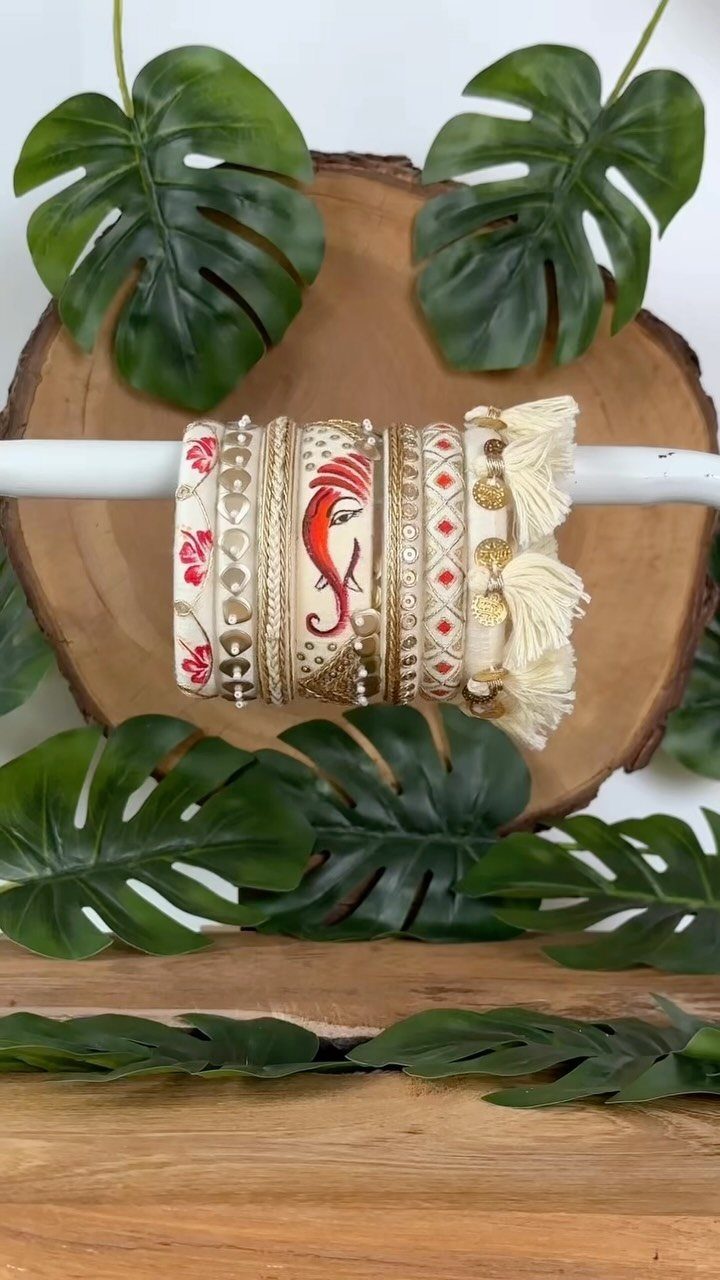 Cream-colored bangles with red and gold painted designs on a white rod.