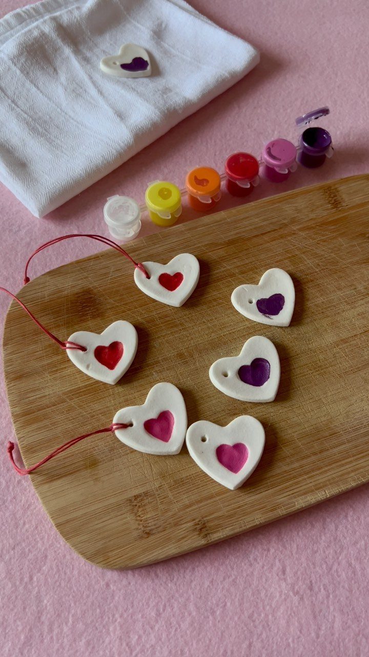White heart-shaped clay ornaments with colorful centers on a wooden board.