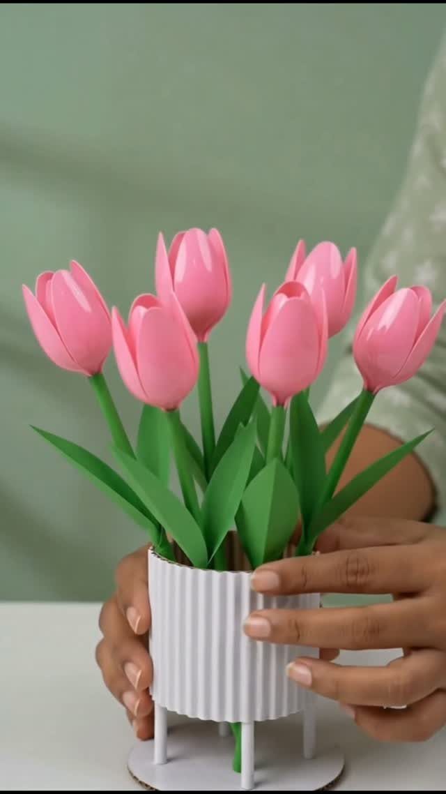 Pink paper tulips in a white corrugated paper pot held by two hands.
