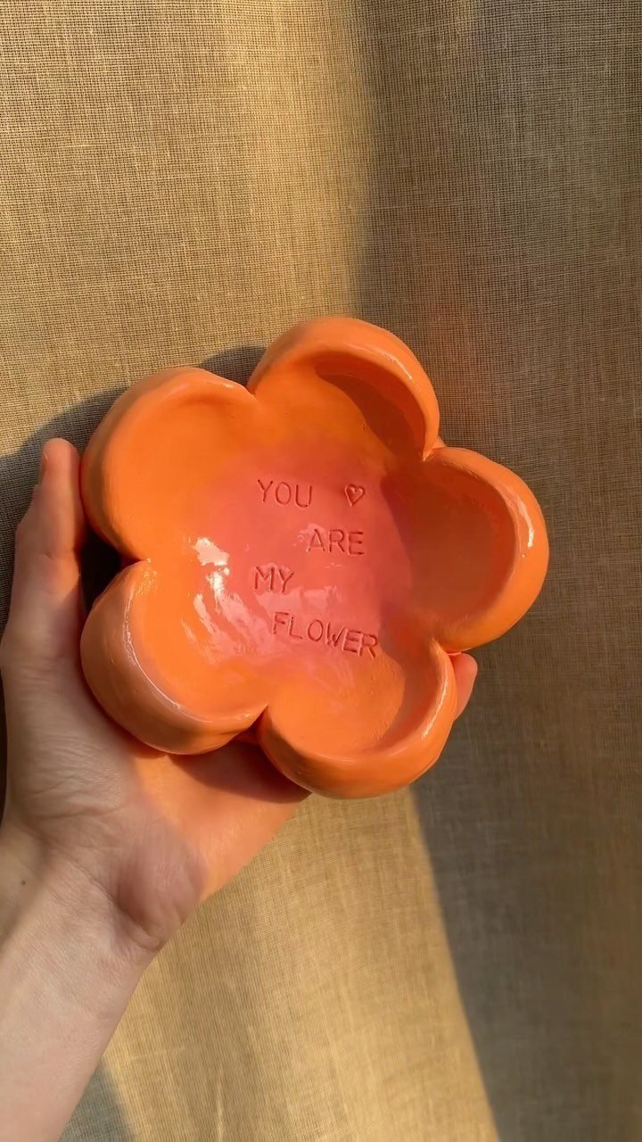 Orange flower-shaped clay trinket dish with embossed text held in a hand.