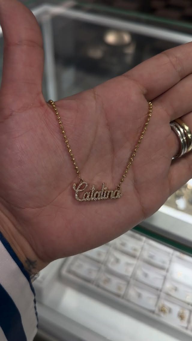 Gold nameplate necklace reading Catalina held in a person's open hand