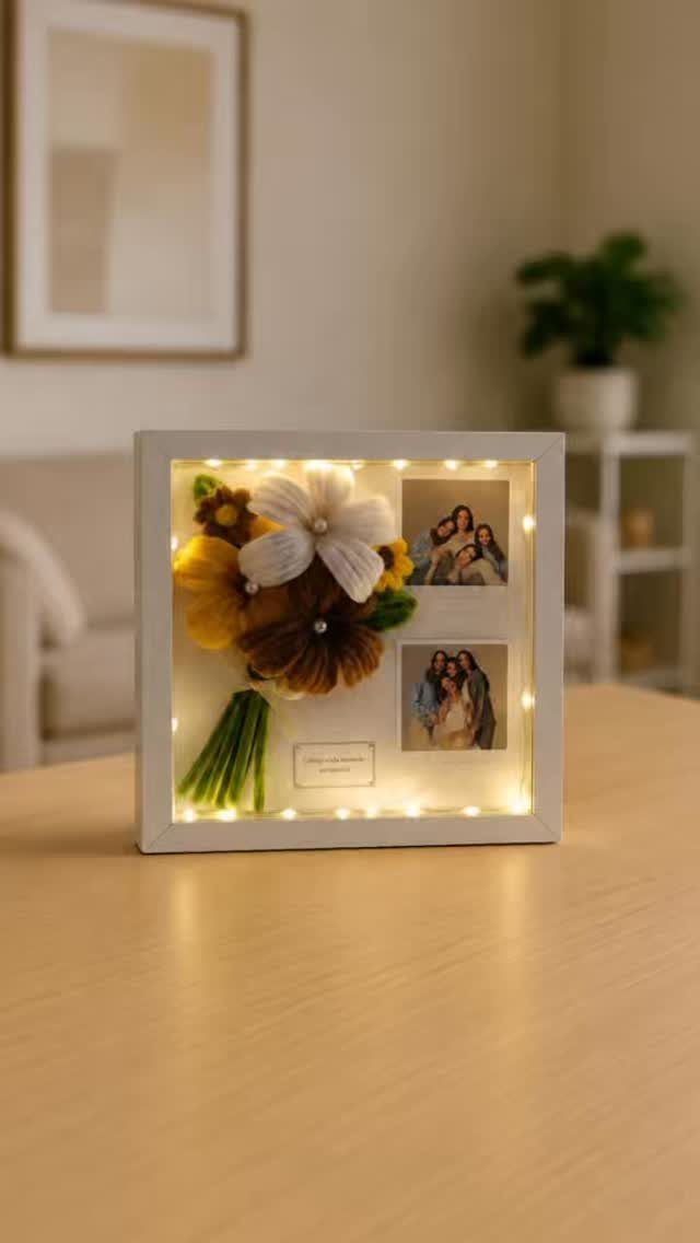 Shadow box frame containing family photos, fabric flowers, and glowing fairy lights.