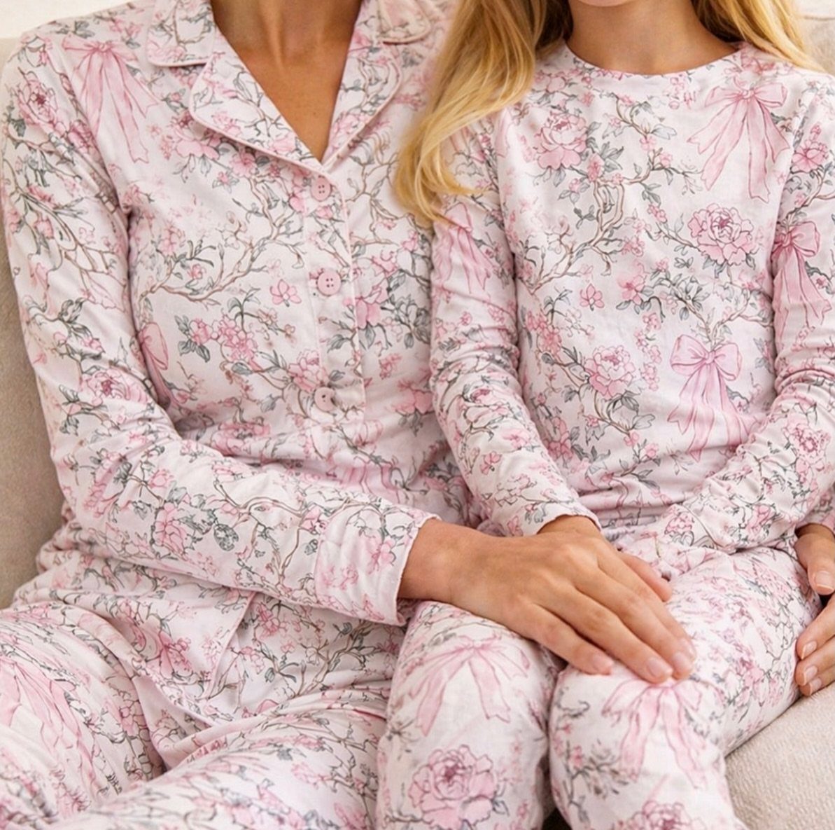 Woman and young girl wearing matching pink floral print pajama sets on a sofa.