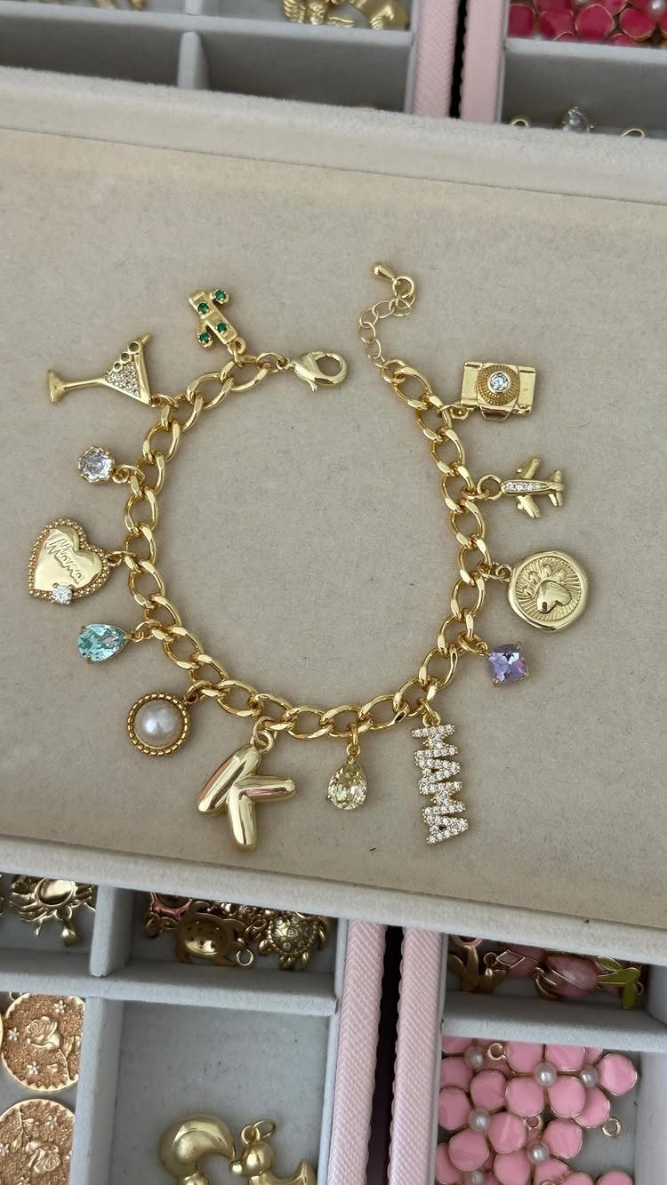 Gold charm bracelet with colorful gemstones and a pearl on a jewelry tray