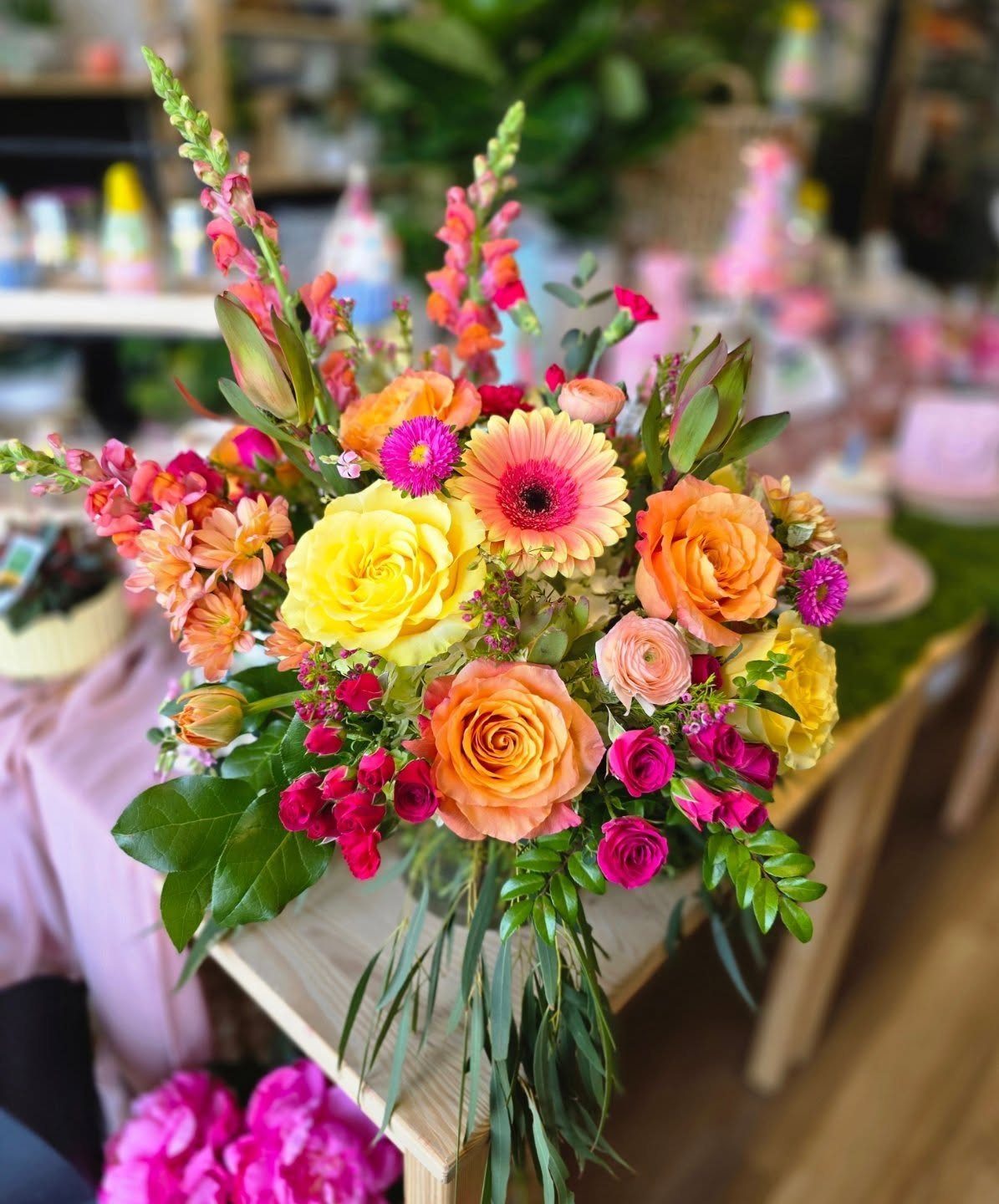 Colorful floral bouquet with yellow roses and orange daisies on a wooden table.
