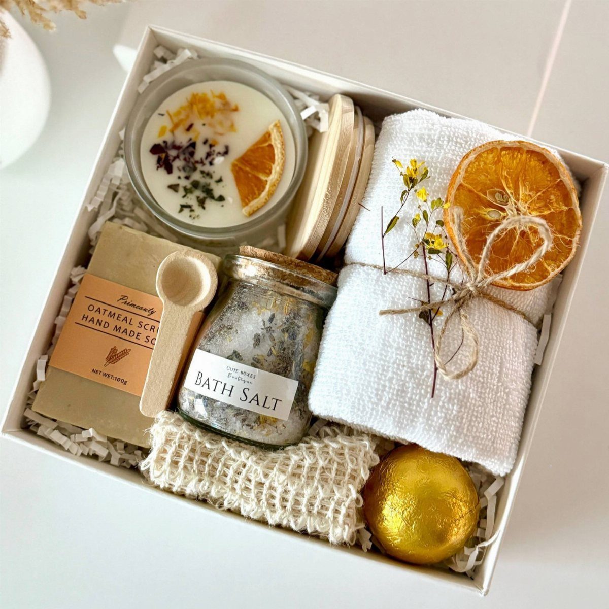 Spa gift box with bath salts, candle, white towel, and gold bath bomb.