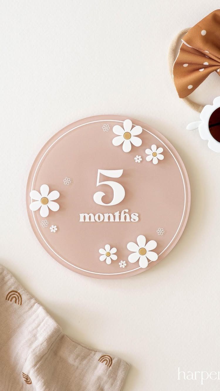 Pink circular baby milestone marker showing five months with white daisy decorations