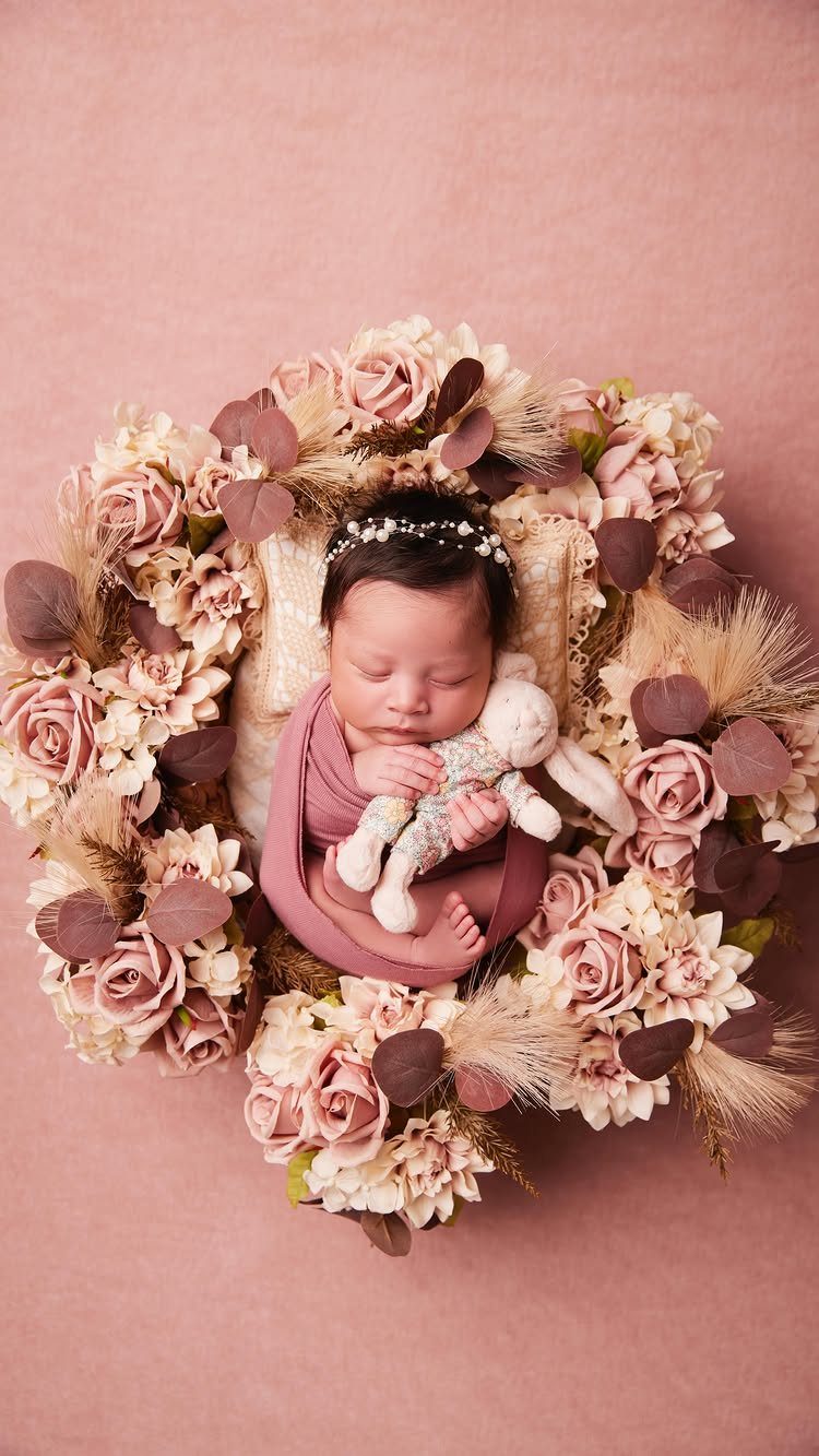 Sleeping newborn baby wrapped in mauve cloth surrounded by a floral rose wreath