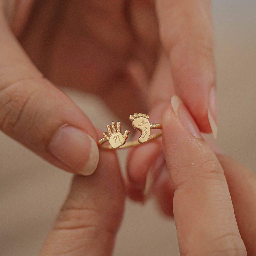 Gold ring with baby handprint and footprint held between two fingers
