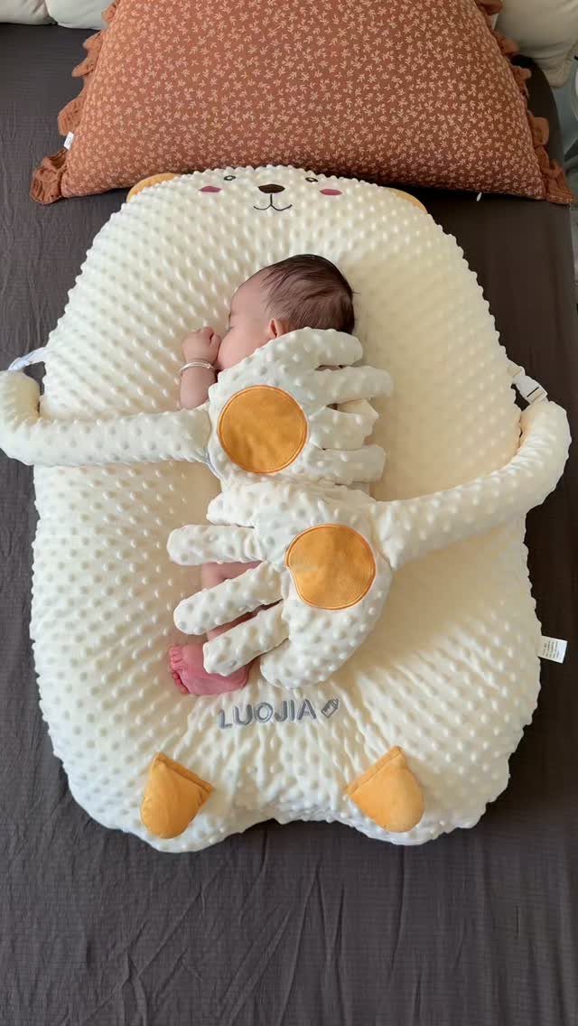 Newborn baby sleeping in a white plush bear-shaped baby lounger on a bed