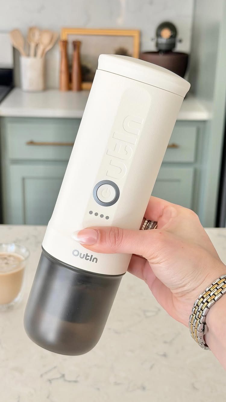 Hand holding a white Outin portable bottle warmer in a bright kitchen setting