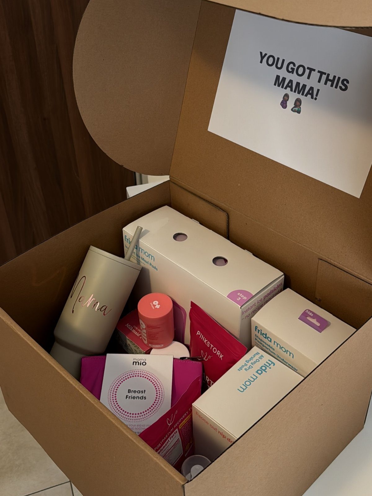 Cardboard gift box containing postpartum care products and a supportive note for a mother