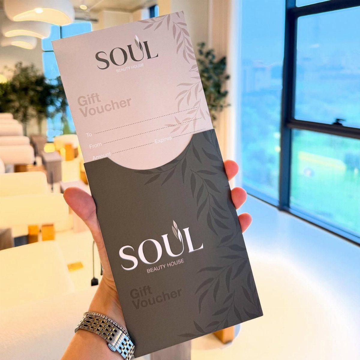 Hand holding a Soul Beauty House gift voucher inside a bright beauty salon.