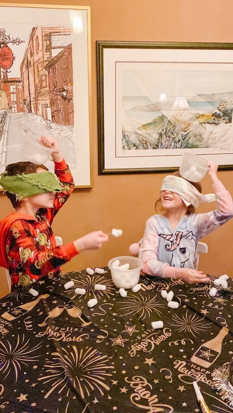 Two blindfolded children playing a marshmallow game on a New Year's themed tablecloth.