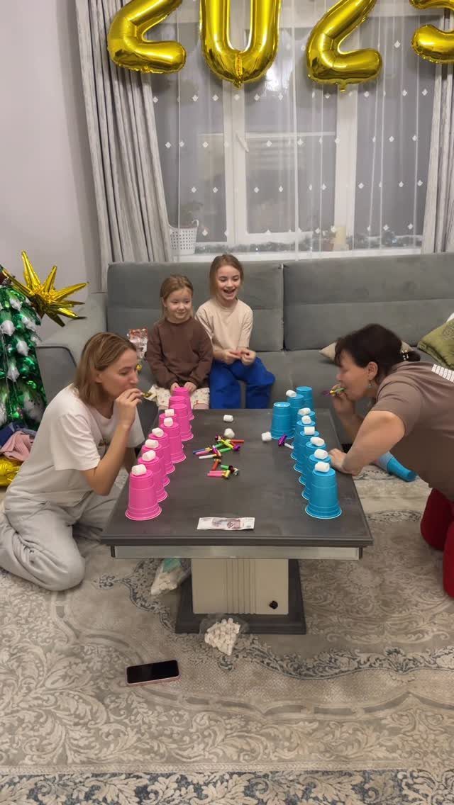 Family playing a cup and ball game in a room with 2023 balloons.