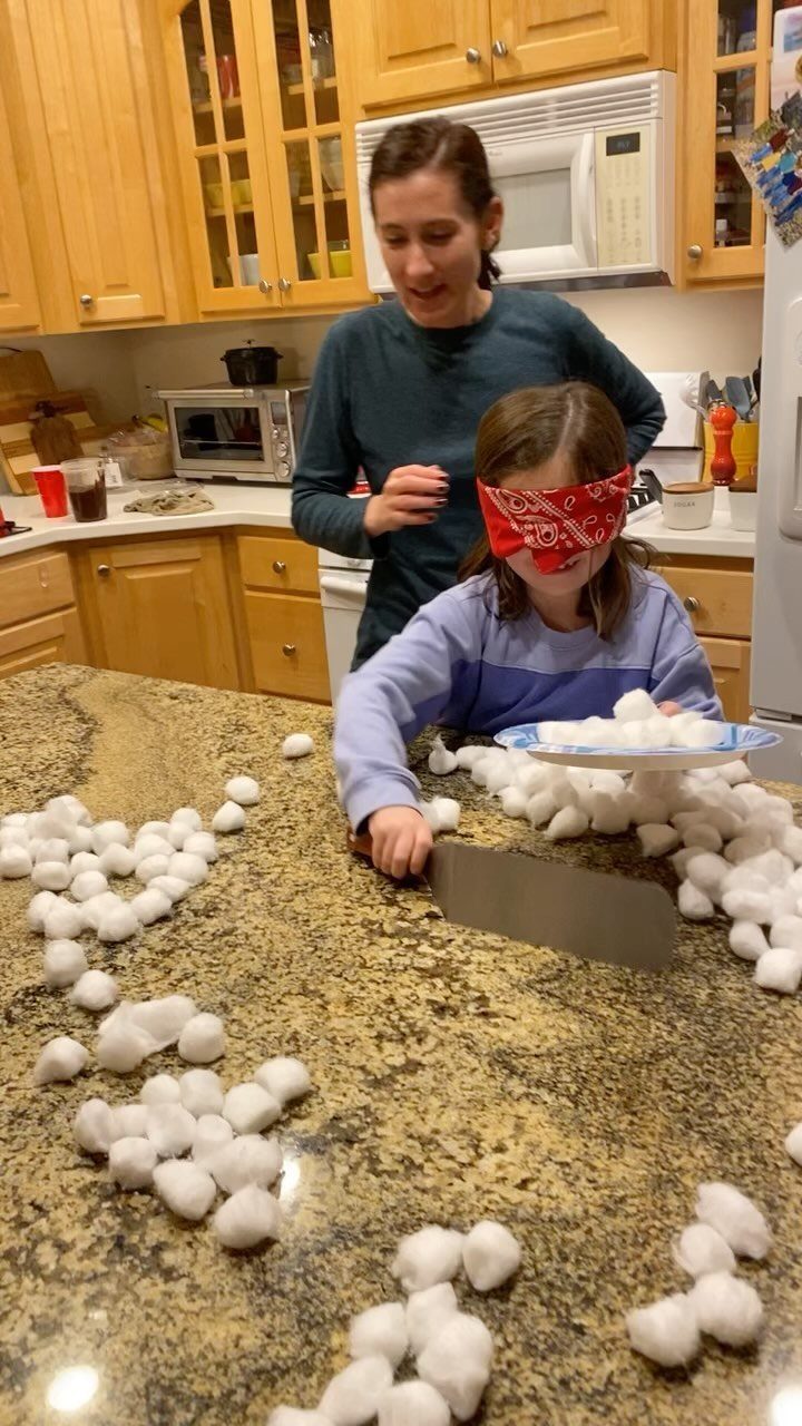Blindfolded girl playing a game with cotton balls on a kitchen counter.