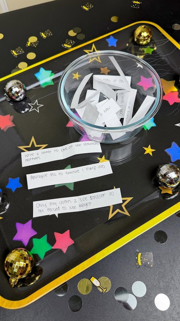 Glass bowl of paper slips on a black table with festive star confetti.