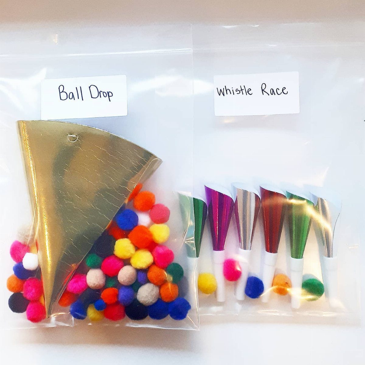 Two party game kits in plastic bags labeled Ball Drop and Whistle Race.