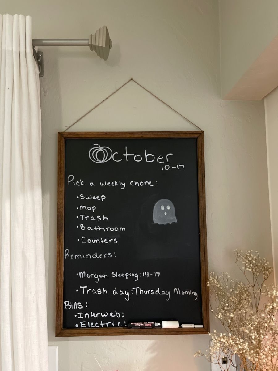 Black chalkboard with wooden frame listing October chores, reminders, and bills with ghost drawing.