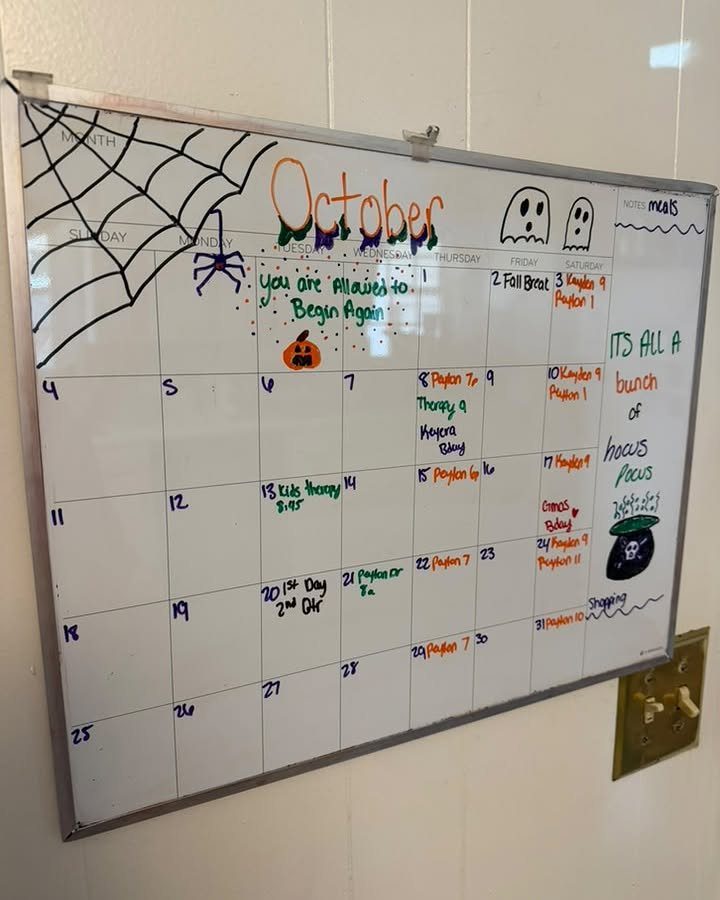October calendar on a whiteboard decorated with a spider web and ghosts.