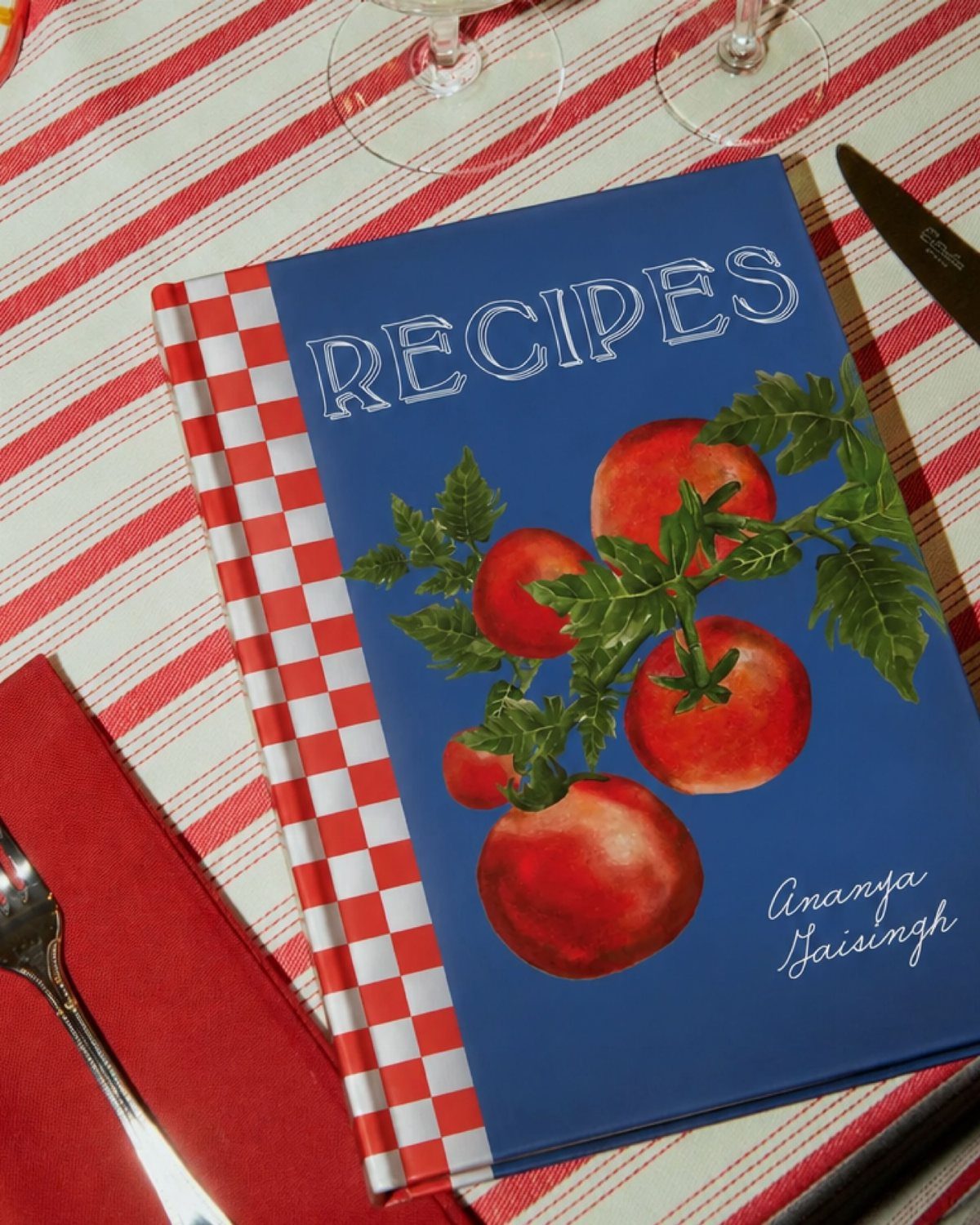 Blue recipe journal with tomato painting on a red striped tablecloth with cutlery
