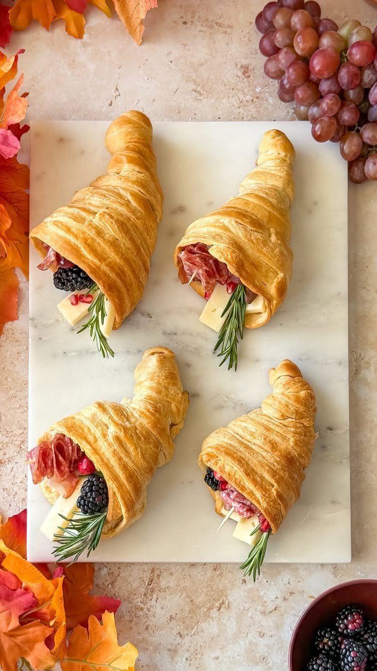 Filled croissants with meat, cheese, and berries on a white marble board.