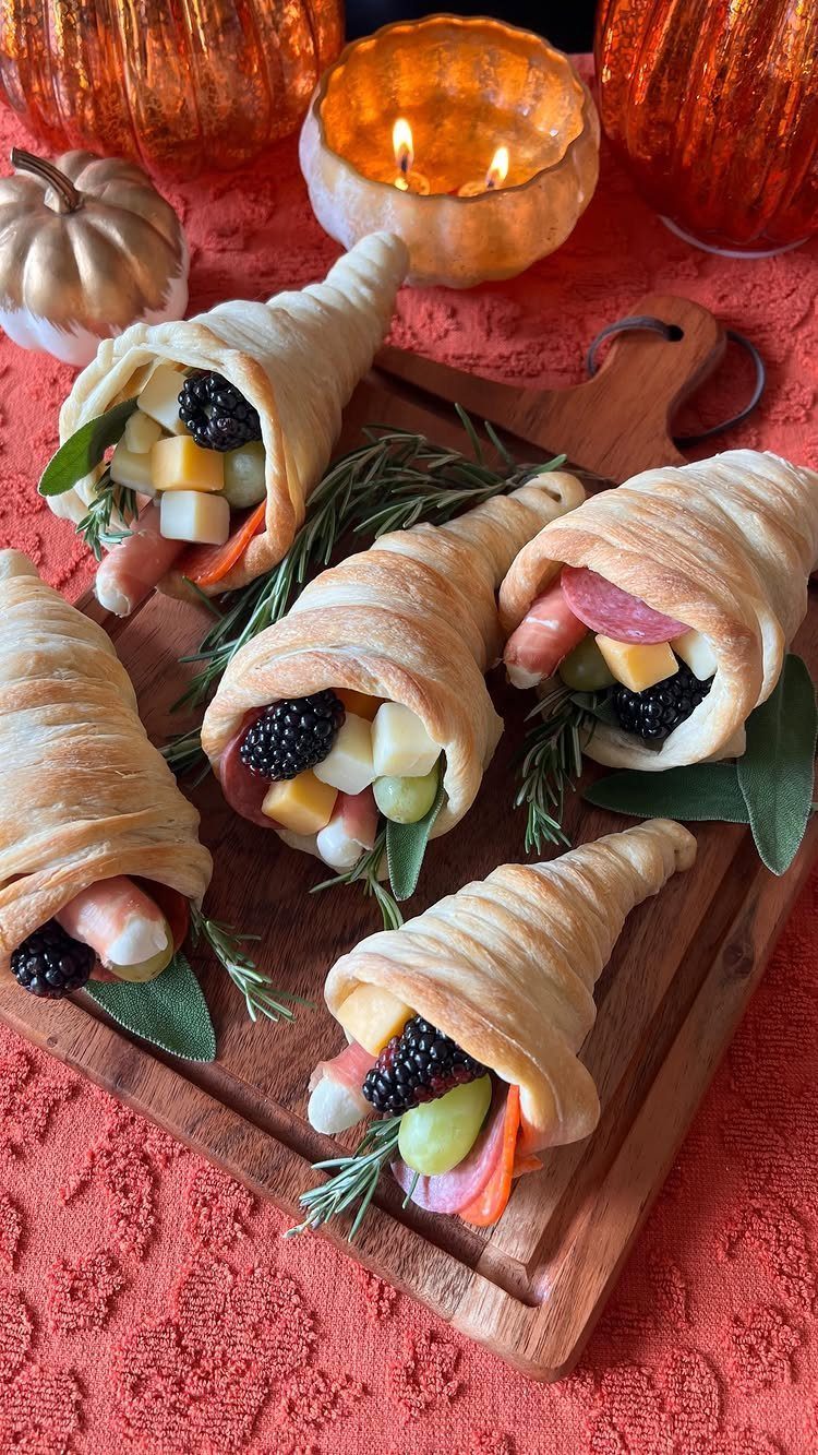 Pastry horns filled with cheese, fruit, and meat on a wooden serving board.
