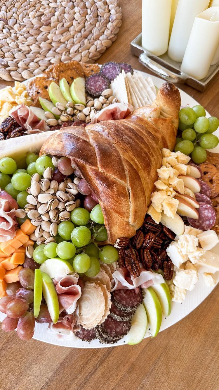 Cornucopia bread centerpiece on a charcuterie board with grapes, apples, nuts, and meats.