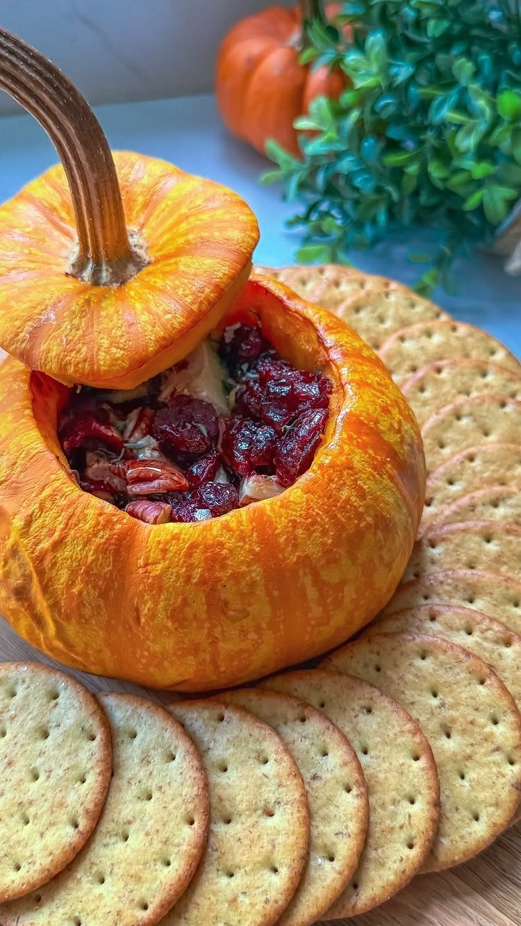 Hollowed pumpkin filled with cranberry dip surrounded by round crackers on wood.