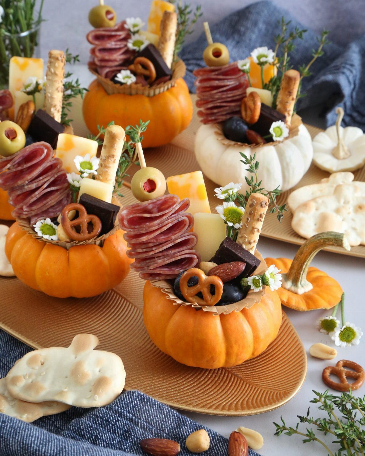 Mini charcuterie boards served inside hollowed-out pumpkins with meats, cheeses, and crackers.