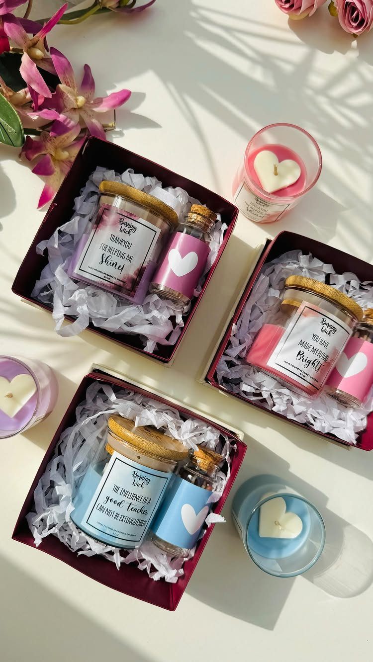 Gift boxes with jars and heart-shaped candles in pink, purple, and blue colors.