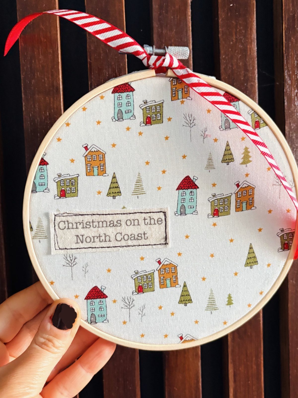 Embroidery hoop with Christmas house fabric and a red striped ribbon.