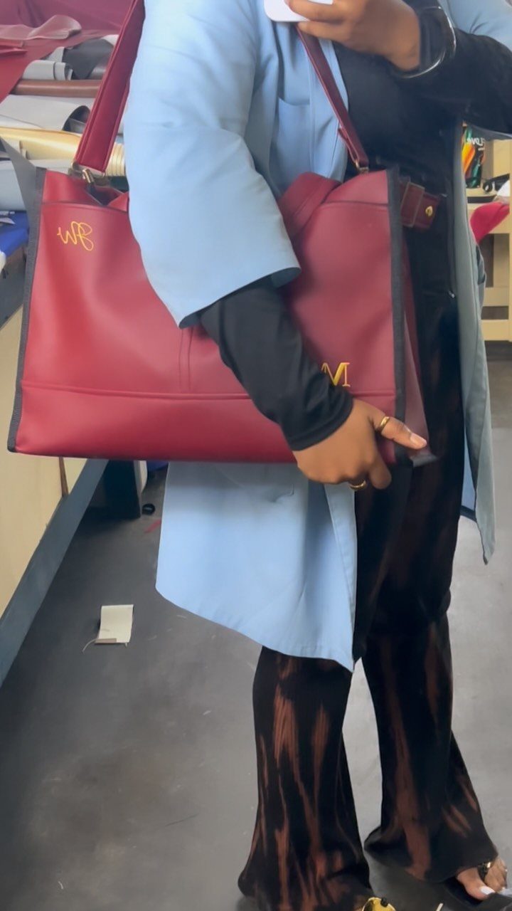 Red leather tote bag with gold monogrammed initials held by a person.